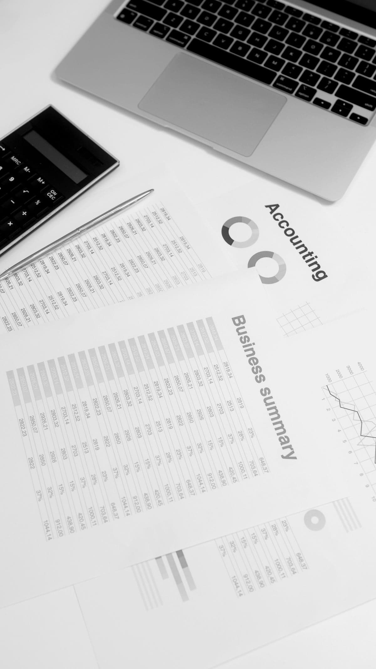A laptop beside monthly accounting statements and reports